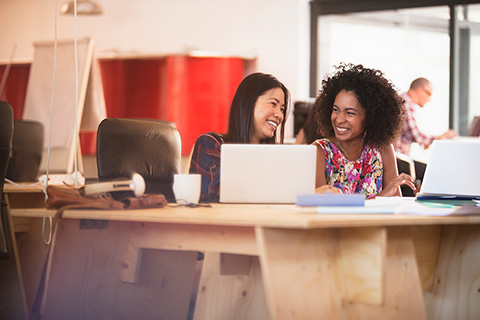 Two friends at computers laughing