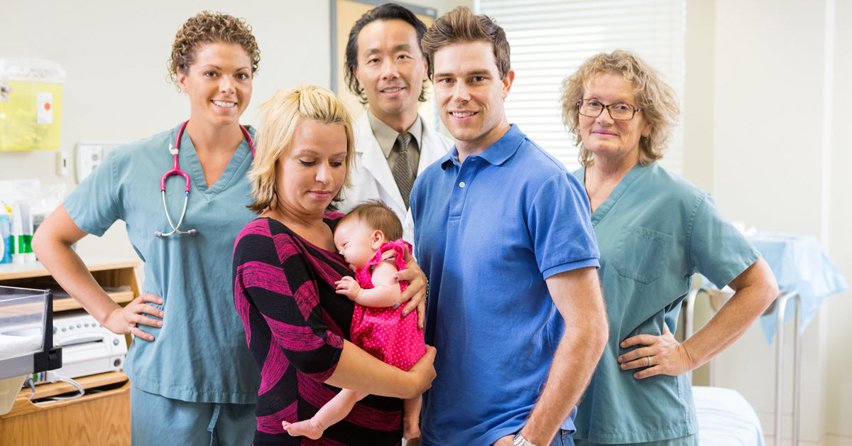 A young mother, baby, and spouse surrounded by three medical professionals