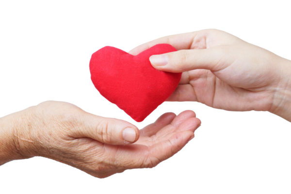 An older hand receiving a red paper heart from a younger hand