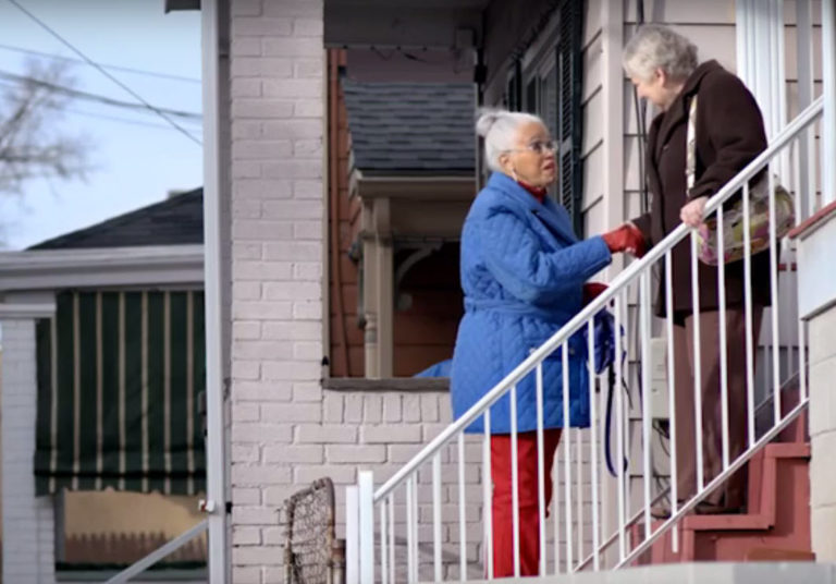 Two older women meeting on the steps outside a house