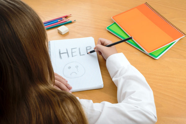 A young girl writing the word “Help” in a notebook