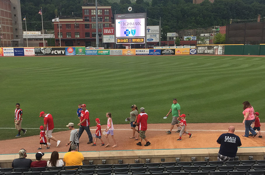 Group of parents and children walking across baseball field with Highmark on the scoreboard in the background