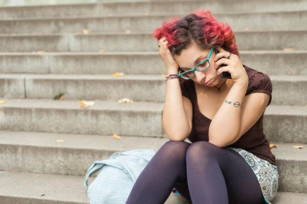 Upset teenage woman sitting on school steps and making a call