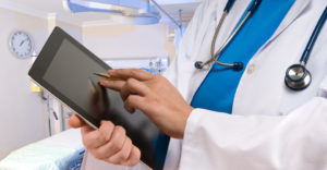 Closeup of a doctor using a tablet device in a hospital room setting